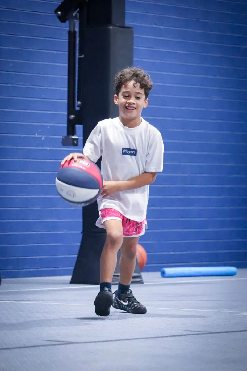 A young boy smiling as he dribbles a basketball